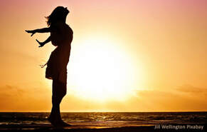 Frau vor Meer und Sonnenuntergang streckt sich und atmet