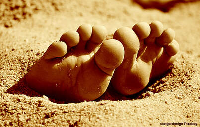 IN HOPE: Zehen ragen aus dem Sand, sonnig